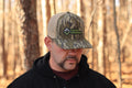 Man wearing a camouflage cap with 'FarmVarmint' logo in a forest setting